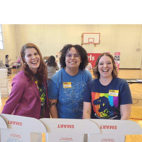 Group of three adult women smiling from behind packaging boxes