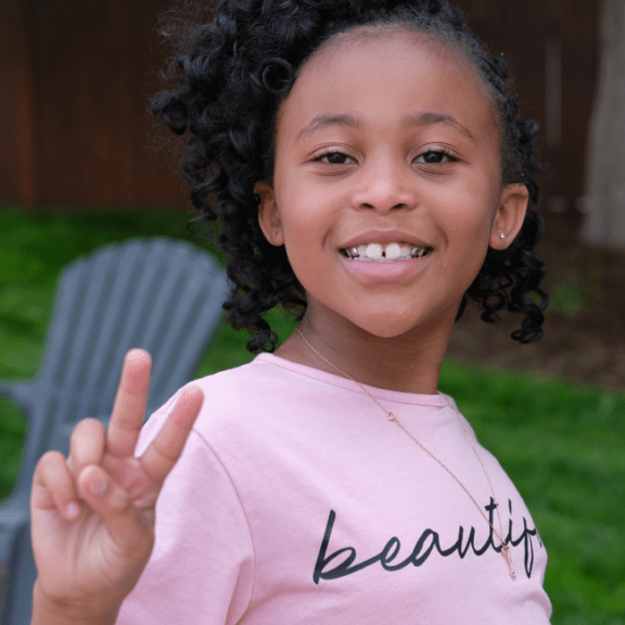 Young girl smiling holding peace sign.