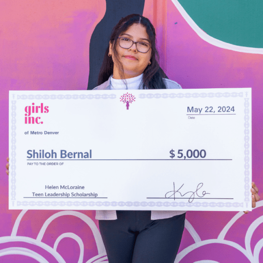 Image of a teen girl smiling and holding a giant scholarship check for $5,000