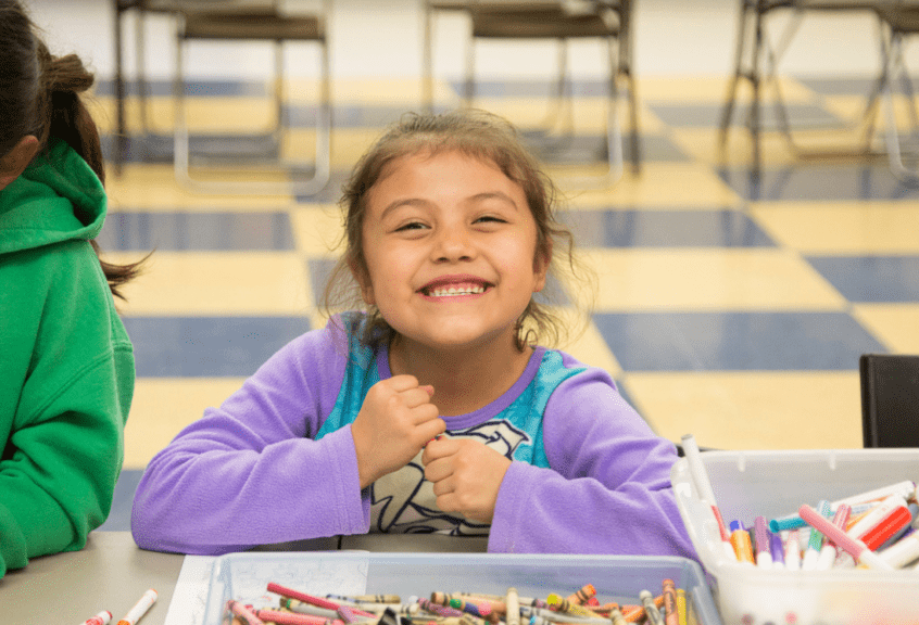 Young girl smiling big with a crayon in her hand.