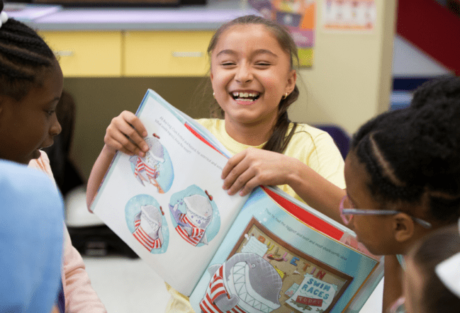 Girl laughing while holding an open book to her friends