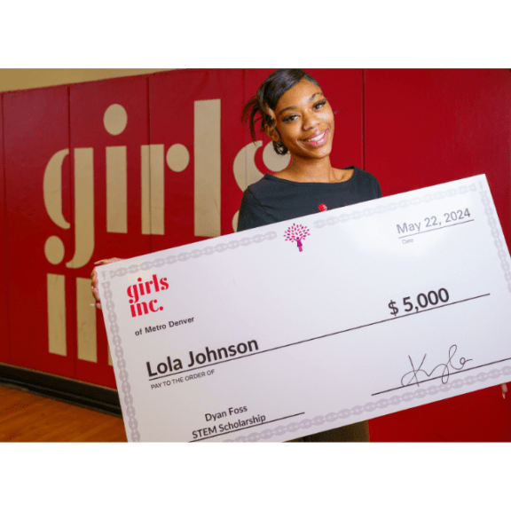 Scholarship winner, Lola, holds up her giant check for $5,000.