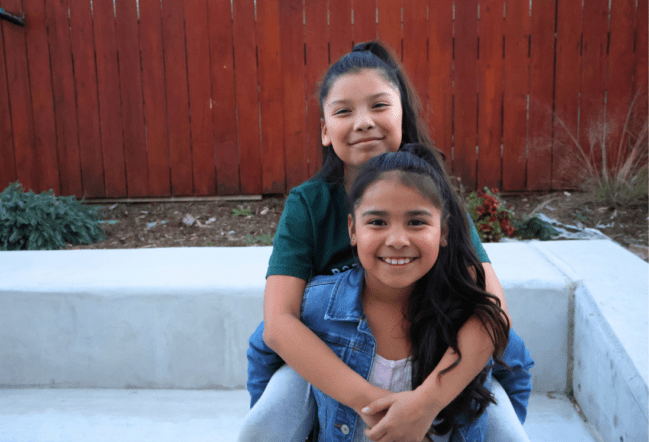 A young girl carrying her friend on her back and smiling.